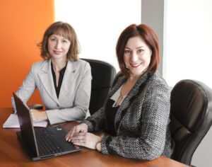 two professional women working in a boardroom with laptop and notebook
