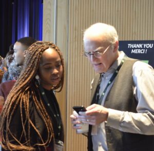 older white man showing something on his mobile device to a black woman with braids at a networking event